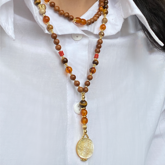 A NECKLACE MADE OF SAUDI GOLD POUND SHELL WITH TIGER-EYE , JASPER , AMBER , CORAL AND COKE WOOD A NECKLACE MADE OF SAUDI GOLD POUND SHELL WITH TIGER-EYE , JASPER , AMBER , CORAL AND COKE WOOD